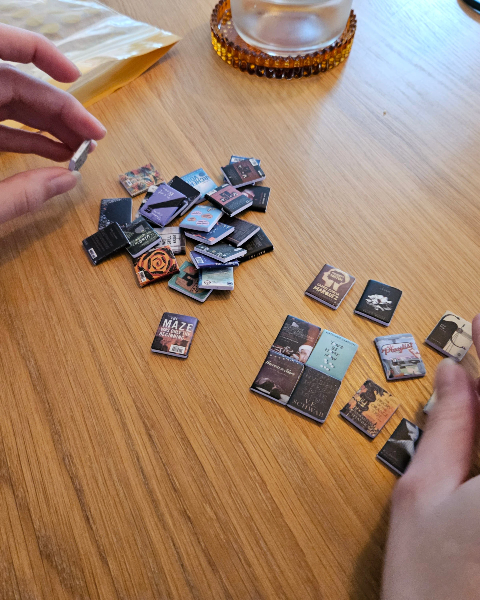 Handen leggen piepkleine fotootjes en boekjes klaar op een houten tafel.