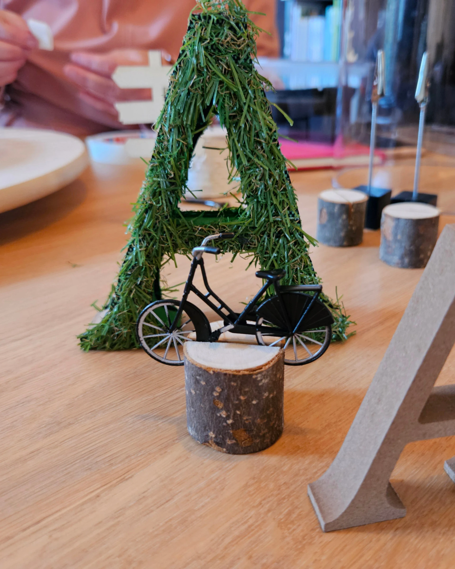 Een letter A van mos met een klein zwart fietsje, naast een houten letter A.