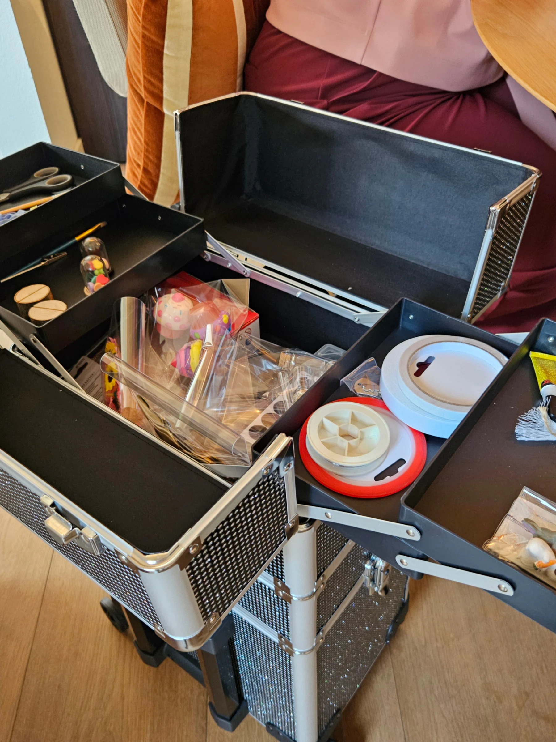 Een opengeklapte koffer met vakjes vol kleine spulletjes, doosjes en materialen.