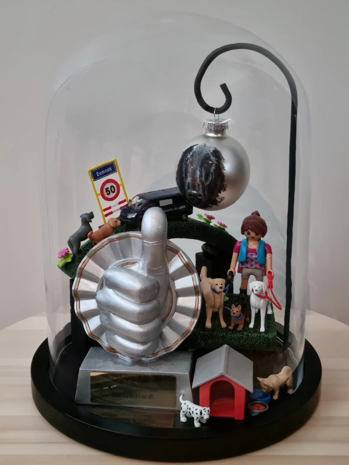 Stolp met een zilveren duim omhoog, een plaatsnaambord Eemnes met 50, een busje, een kerstbal met een hondenkop, een speelgoedvrouw met honden en een hondenhok.