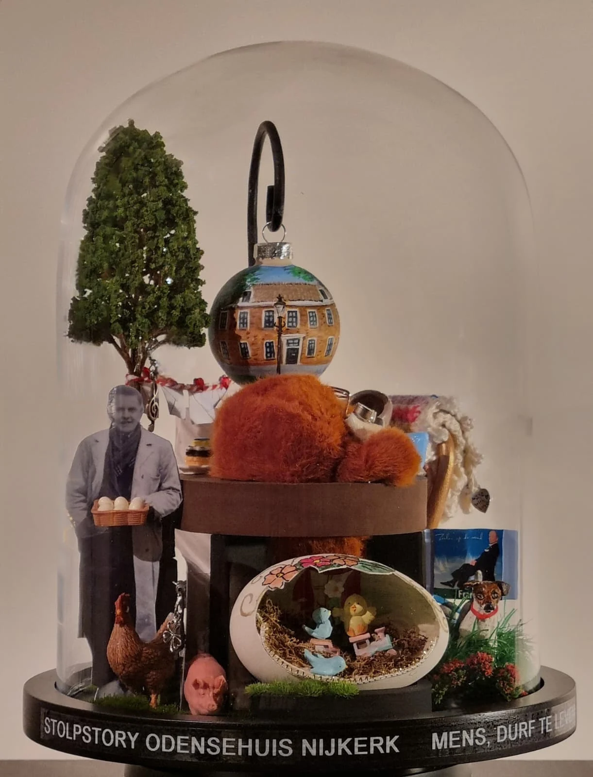 Stolpstory voor het Odensehuis in Nijkerk, met een boom, een man met een doos eieren, een kip, een hondje en een beschilderde kerstbal met een huis.