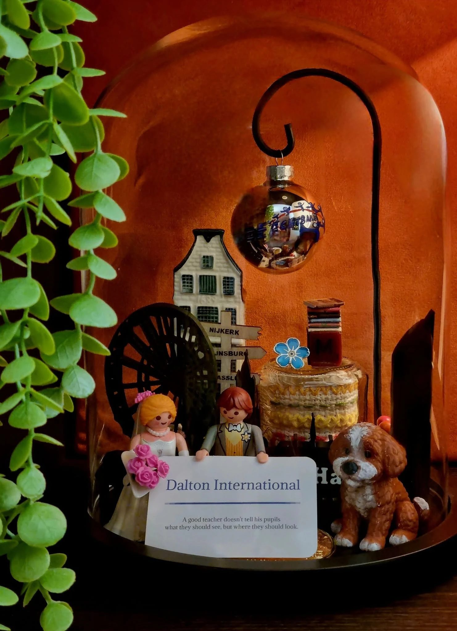 Stolp tegen een oranje muur met een speelgoed bruidspaar, een hondje, een grachtenpandje, een kerstbal en een kaartje van Dalton International.