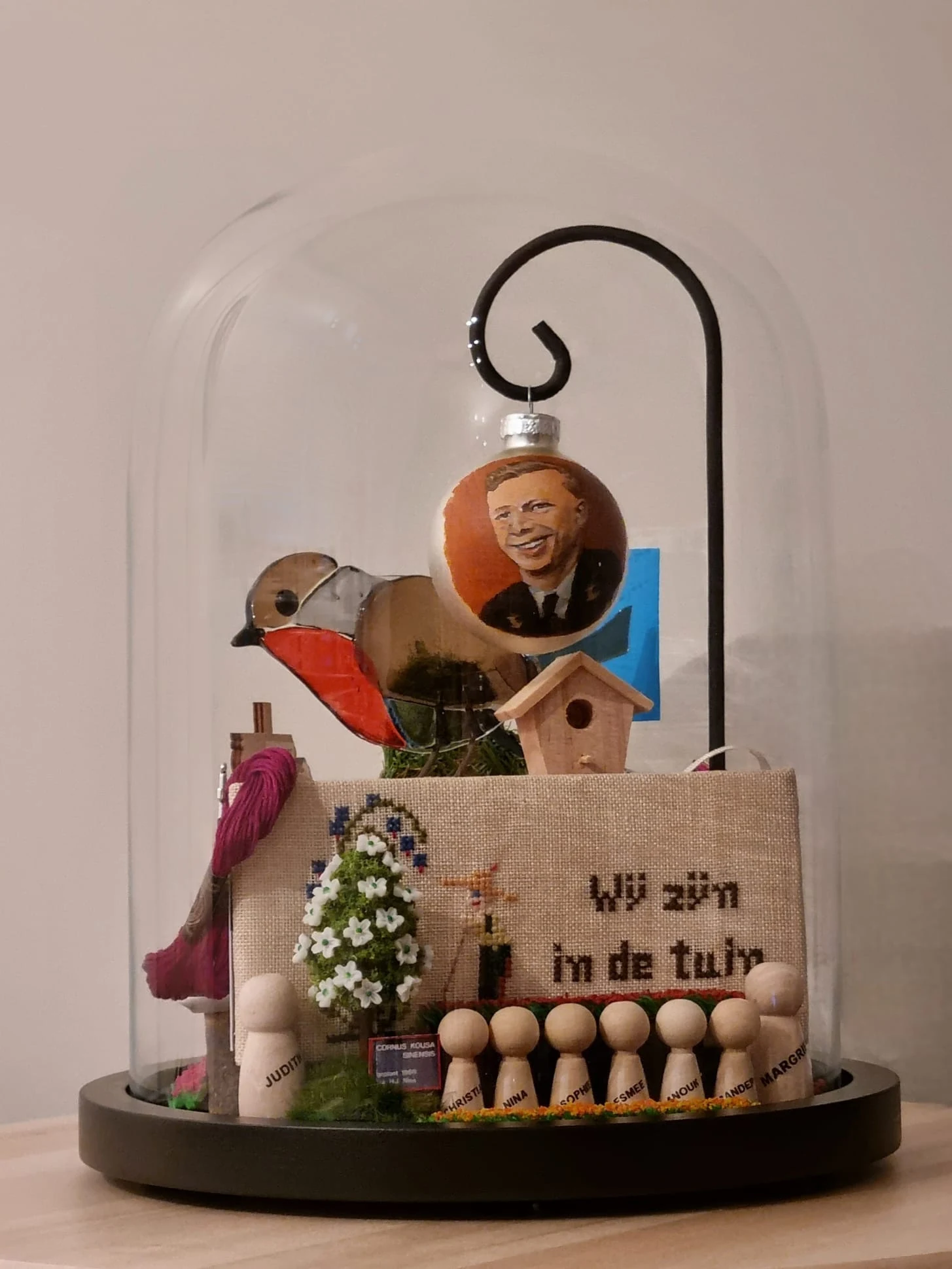 Stolp met een roodborstje, een kerstbal met een portret, een geborduurd lapje 'Wij zijn in de tuin', een vogelhuisje en houten poppetjes.