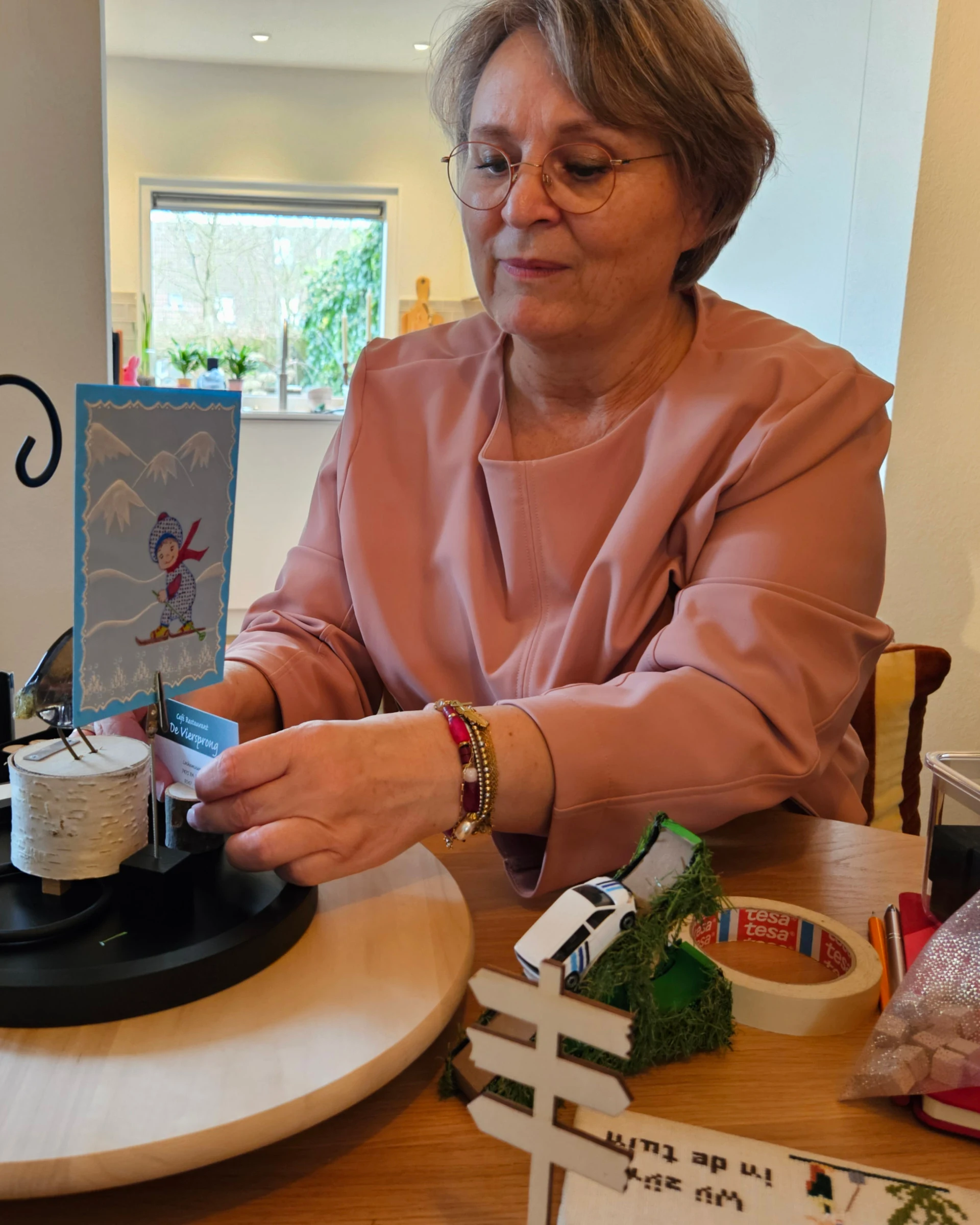 Wendy zet aan tafel een tekening van een schaatser op de voet van een stolp, op een houten draaiplateau.